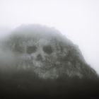 Vygenerováno pomocí umělé inteligence DALLE-2 dotazem: Old black and white photo of a mountain covered with fog in shape of a skull. Temná hora zahalená mlhou ve které je vidět obrys lidské lebky.