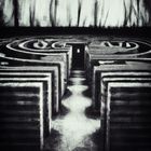Vygenerováno pomocí umělé inteligence DALLE-2 dotazem: Old black and white photo of a dark labyrinth with strange geometry. Labyrint s podivnou geometrií s tmavými dveřmi uprostřed.